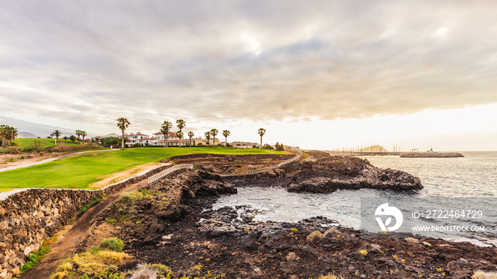 Ground path with handrails and golf course along rocky coastline. Tenerife, Spain.