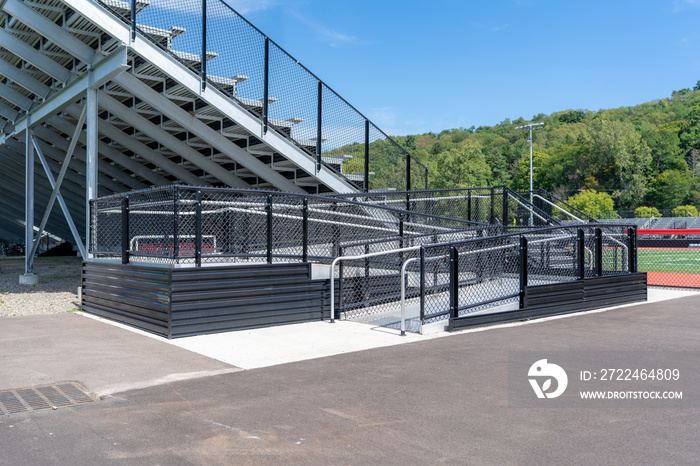 Accessible wheelchair ramp with railings and slip resistant surface at empty metal stadium bleacher.  Nondescript location with no people in image.  Not a ticketed event.