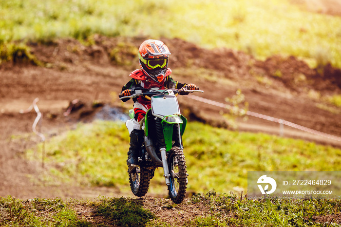 Racer child on motorcycle participates in motocross cross-country in flight, jumps and takes off on springboard against sky. Concept active extreme rest teenager.