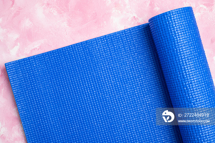 Blue yoga mat on pink background. Equipment for yoga. Concept healthy lifestyle, sport, meditations and relaxations. Top view, copy space