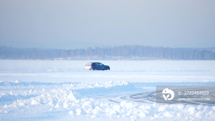 Winter driving. Blue car drives by icy track on snow covered lake at winter. Sport car racing on snow race track in winter. Driving a race car on a snowy road