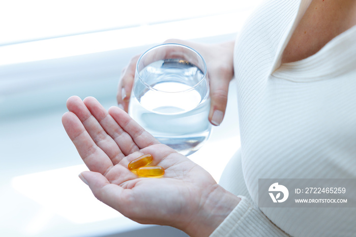 Close up of woman holding vitamin capsules and glass of water. Nutritional Supplements. Capsules vitamin and dietary supplements..