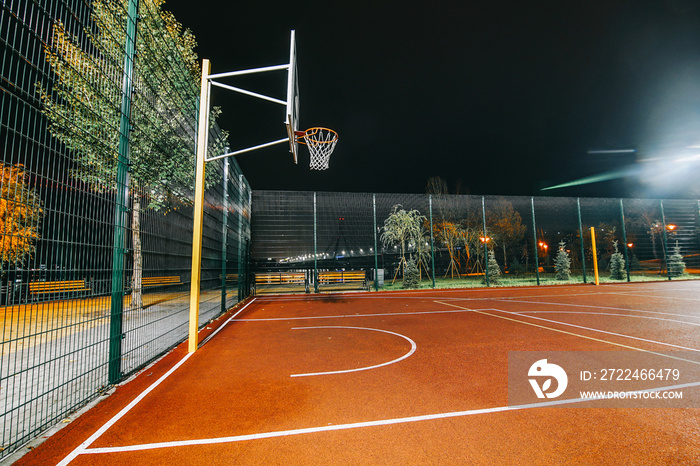 Illuminated basketball playground with red pavement, modern new basketball net and lens flares on background.