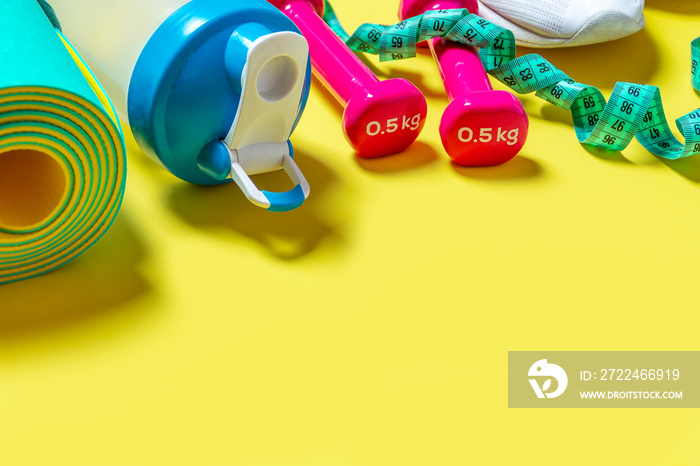 Flat Lay Sport and fitness equipment, measuring tape, pink dumbbells, white sneakers, water blender bottle and mint yoga mat on yellow background. Top view with copy space. Healthy lifestyle