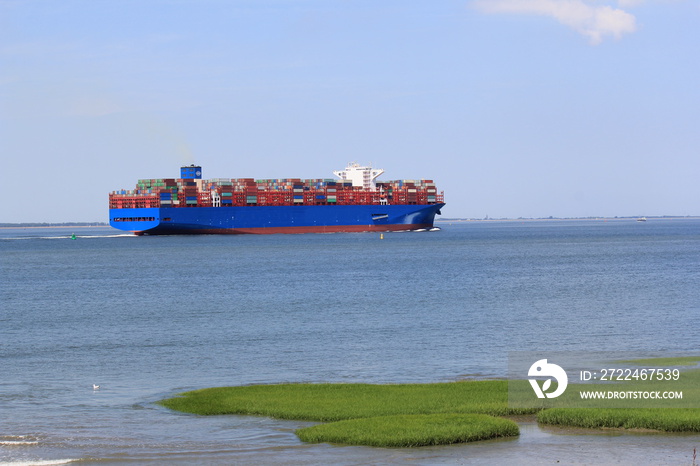 a large container ship navigates through the westerschelde sea towards antwerp along green grass humps in the salt marsh