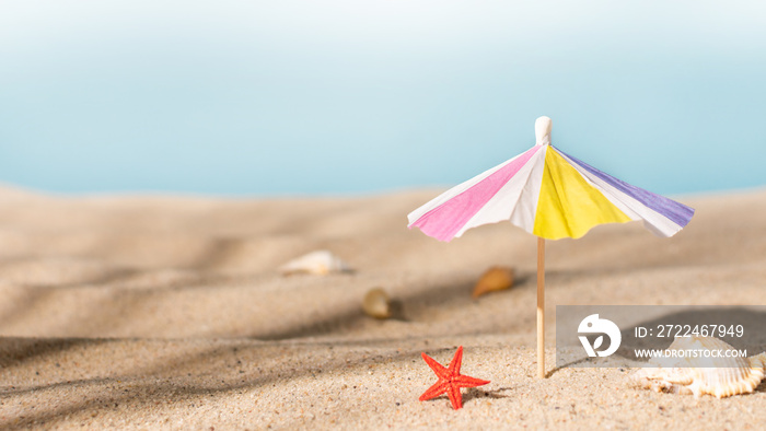 Sunshade umbrella on a sandy beach with seashells. Summer vacation concept.Summer background.