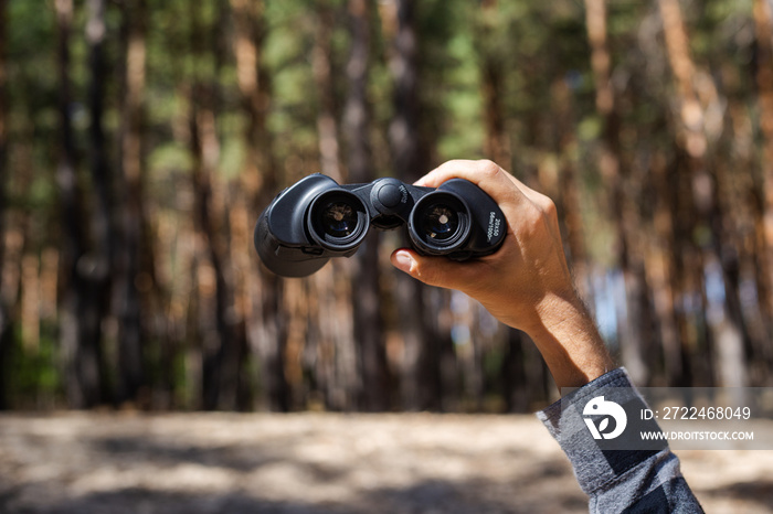 Male hand hold binoculars on the background of the forest. Banner. Flat lay, top view