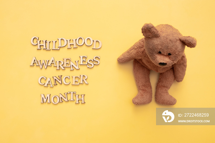 Childhood cancer awareness month text from wooden letters and teddy bear on yellow background