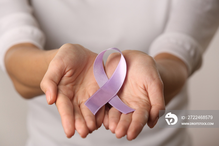 Close up view of female hands holding lavender ribbon. Cancer and epilepsy concept