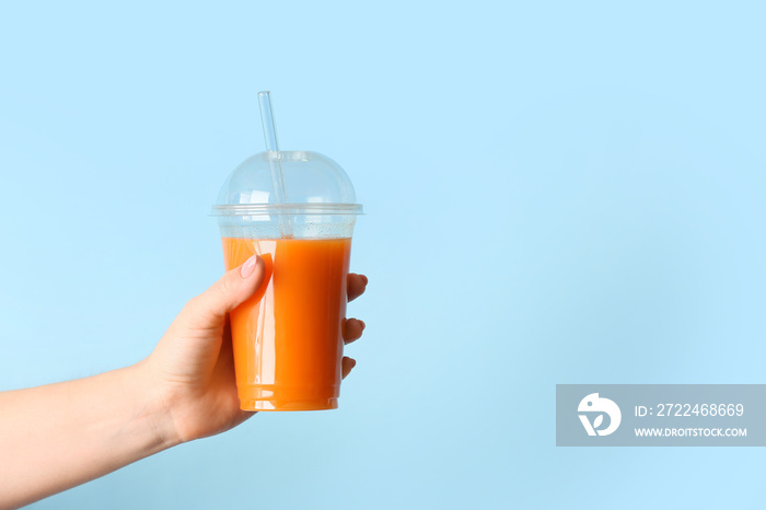 Female hand with plastic cup of healthy juice on color background