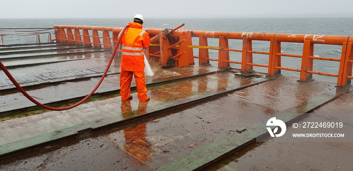 a sailor washes the deck of a ship with the pressure of sea water from a fire hose