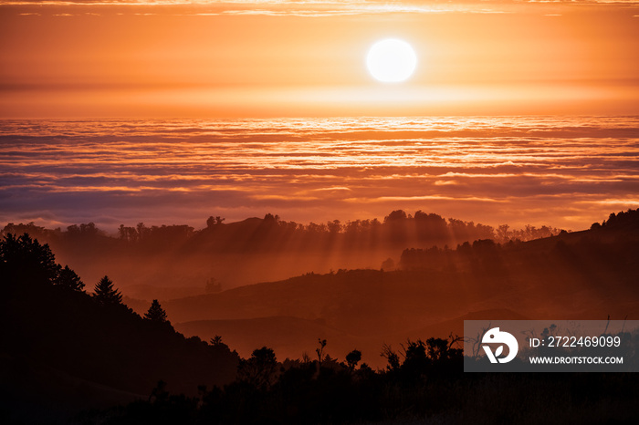 Brightly colored sunset in the Santa Cruz mountains, layered hills and valleys visible in the foreground and sea of clouds in the background; San Francisco Bay Area, California