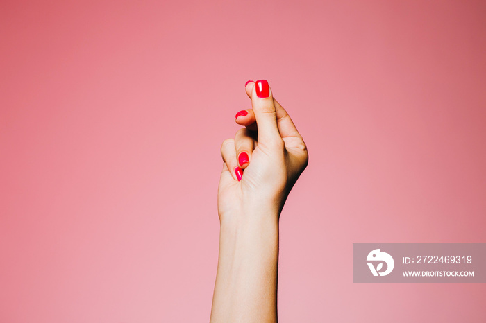 Woman’s snapping hand with bright manicure isolated on pink background