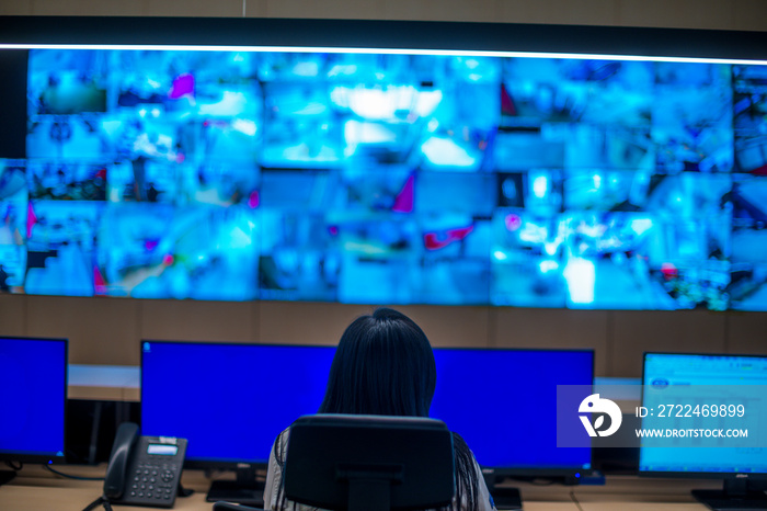 Female security guard sitting back and monitoring modern CCTV cameras in a surveillance room.