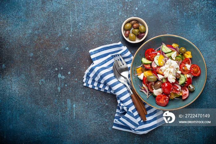 Greek fresh healthy colorful salad with feta cheese, vegetables, olives in blue ceramic bowl on rustic concrete background top view, Mediterranean diet, traditional cuisine of Greece. Space for text