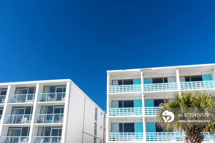 Turquoise and white mid century modern motels on the beach with a cloudless blue sky.