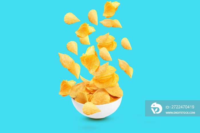 Many tasty potato chips falling into bowl on light blue background