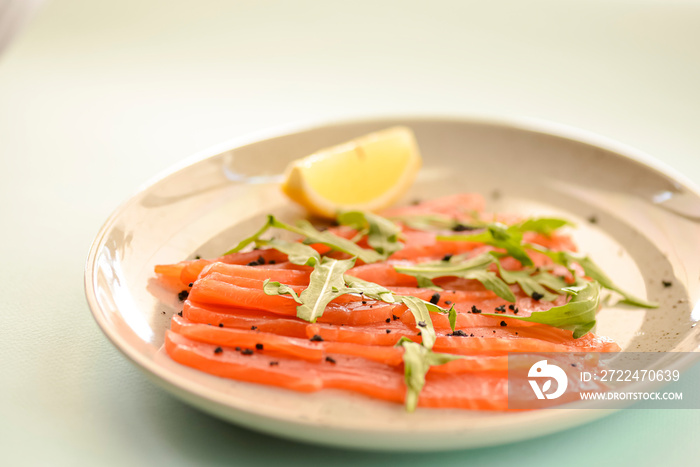 Close-up of smoked salted salmon served with herbs and lemon on a white plate with blue mint background.