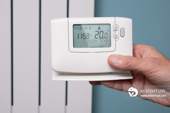 Hand holding central heating controller with modern radiator panel in background