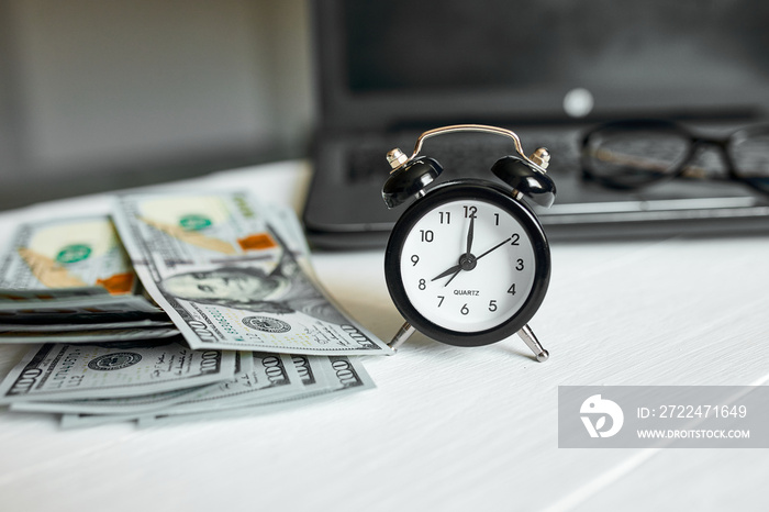 Modern workplace of laptop, clock, money, dollars banknote with copy space on white wooden background. Time for money.