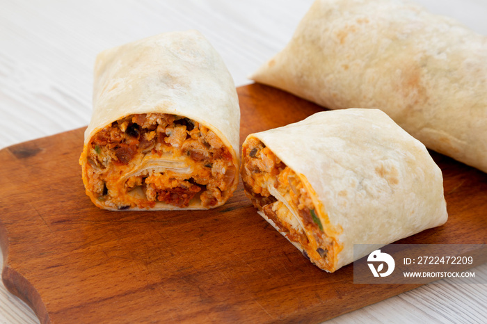 Homemade chorizo breakfast burritos on a rustic wooden board on a white wooden surface, low angle view. Close-up.