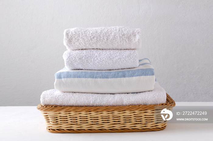 Stack of fresh clean towels in the wicker basket on the white table against bright wall