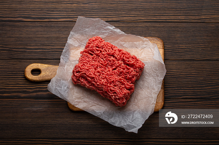 Fresh raw minced meat from ground beef or pork on cutting board and dark brown rustic wooden background from above for catalog or shop