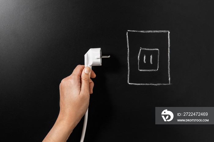 electricity, energy and power consumption concept - close up of hand holding plug near socket drawing on black chalkboard background