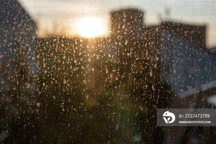 Dirty window glass with dust and dried raindrops backlit with a sunset light on a blurred background of city outlines. Dirty glass lit by the sun. Texture. Front view.