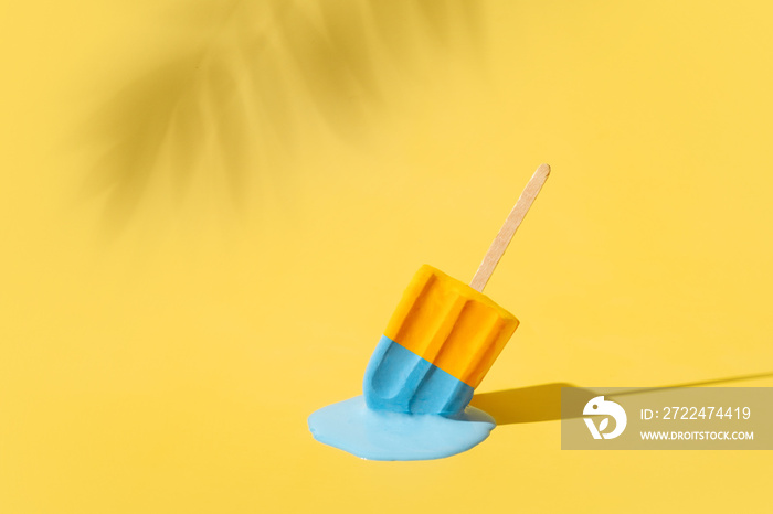 Colored yellow and blue ice cream melts from the hot sun. Palm leaves shadow. Hot weather concept