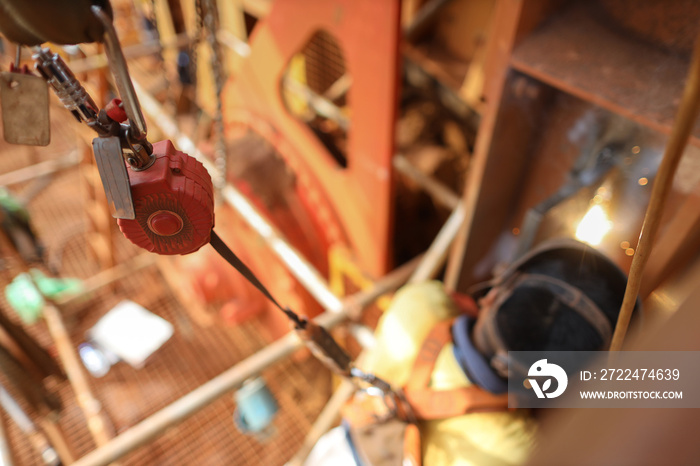 Top view welder wearing safety helmet fall arrest harness using fall prevention system red fall arrester retractable energy shock absorber lanyard device attached on two tone lifting sling