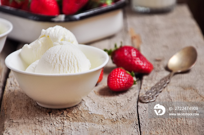 Vanilla ice-cream in a white small bowl with fresh ripe strawberries on a wooden background. Rustic style and close up. Summer food concept.