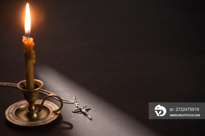 church candle in candlestick burning near catholic cross in dark with sunlight