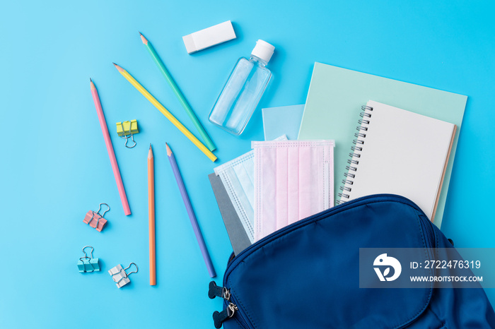 Blue backpack with stationery over blue table background.