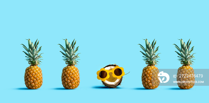 One out unique coconut wearing sunglasses with many pineapples