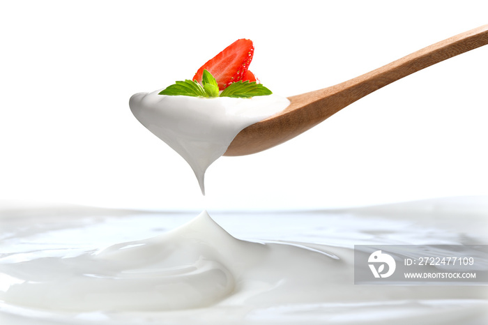 Plain yogurt on a spoon with fresh  strawberry on top hanging above of plain yogurt isolated on white background