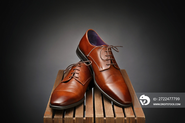 Pair of leather male shoes on wooden box against dark background