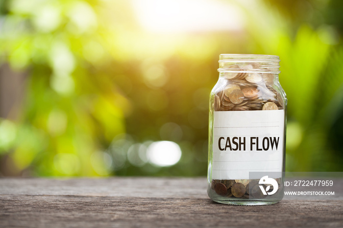 cash flow word with coin in glass jar on wooden table.