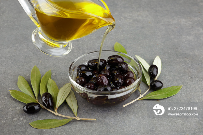 Olive oil in glass with black olives and leaves on rustic background