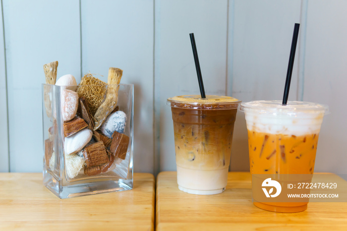 close up of iced latte coffee and thai tea in transparent plastic glass and straw on the wooden table. coffee and cafe decoration concept.