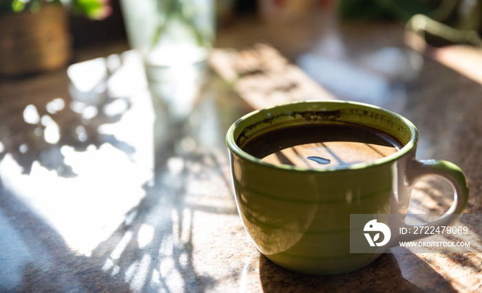 A cup of coffee. The rays of the morning sun shining on a cup of black coffee with foam. A stimulating drink with caffeine.