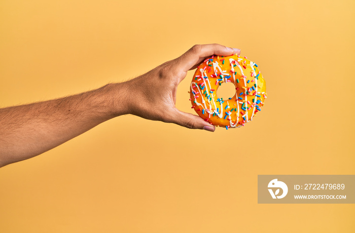 Hand of hispanic man holding donut over isolated yellow background.