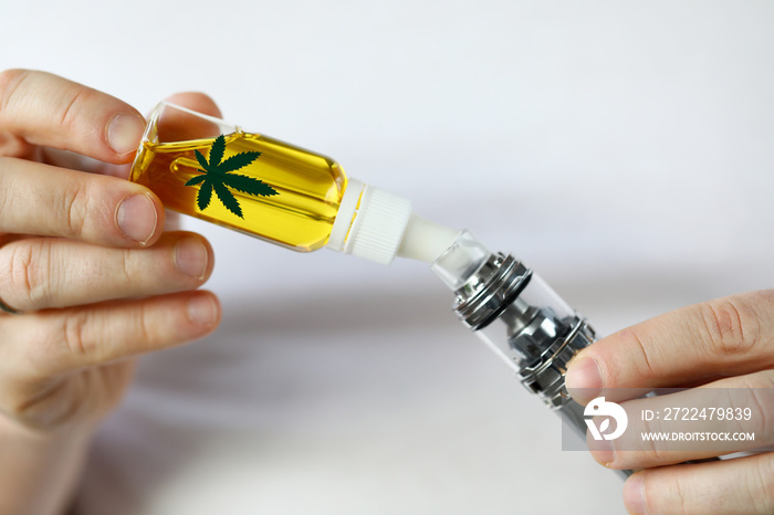 Male hand fill up liquid organic extra virgin cannabinoid oil with vipe pen system against home background. Medical marijuana treatment concept