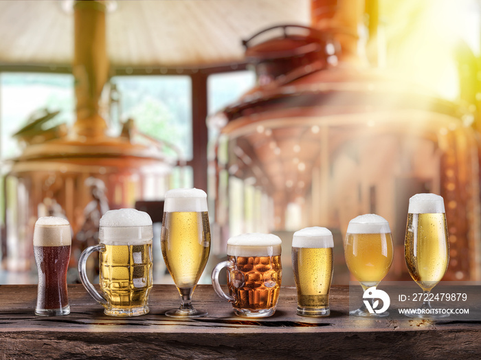 Beer glasses on wooden table and copper brewing cask at the background.