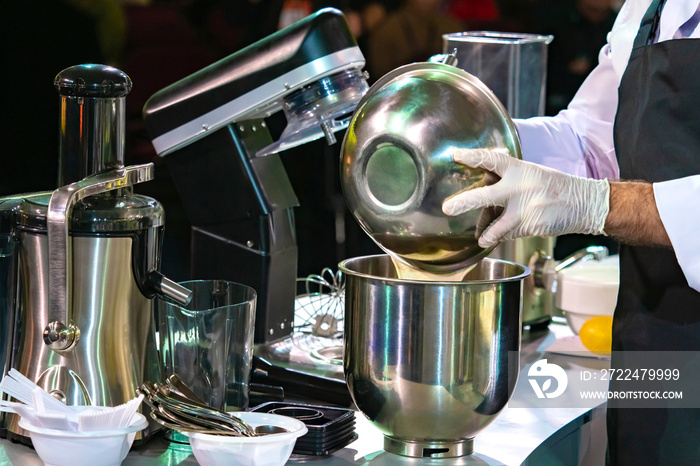 Pastry chef prepares the dough. Work with an industrial mixer. Confectioner pours liquid into a blender bowl. Equipment for the confectionery workshop. Process of making a dessert.