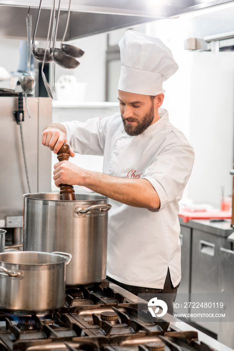 Chef cook in uniform peppering soup in the big cooker at the restaurant kitchen