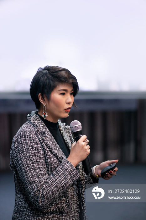 asian woman speaking over white screen in seminar