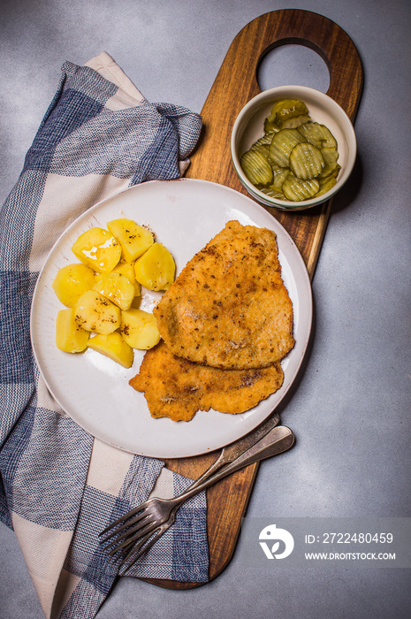 Chop pork cutlets , served with boiled potatoes and salad of pickled cucumbers on wooden board. A typical Polish dinner (kotlet schabowy).