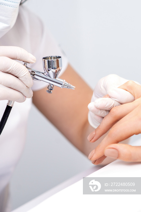 Young woman receiving manicure by airbrush in nail salon. Procedure for spraying paint on the nails