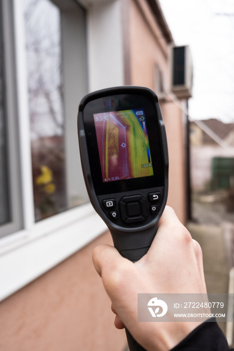 A male hand holds a thermal imager at the window of a house. Search for heat loss in private houses.